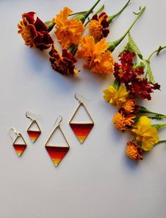 three pairs of earrings sitting on top of a white surface next to flowers and yellow carnations