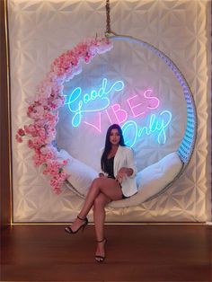 a woman sitting in front of a neon sign that says good vibes only on it