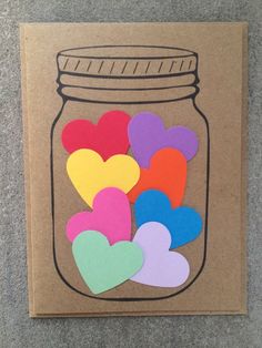 a jar filled with paper hearts on top of a brown card board next to a gray wall