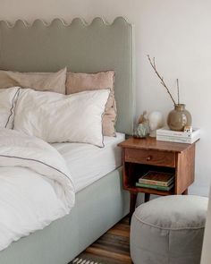 a bed with white sheets and pillows on top of it next to a small table