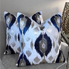 two blue and silver pillows sitting on top of a couch