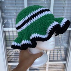 a hand is holding up a green and white hat on a mannequin head