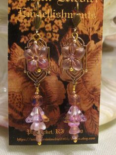 Edwardian elegance is revisited in this  pair of Art Nouveau earrings. Reproduction brass stampings form the base of the earring.  A Czech glass flower bead is dropped from the ear wire, followed by more Czech glass baby bell beads and filagree bead caps. Your choice of pink or green. FREE shipping in the continental USA!! FREE gift wrapping upon request. Handmade Czech Glass Vintage Flower Earrings, Handmade Czech Glass Flower Earrings In Vintage Style, Handmade Vintage Czech Glass Flower Earrings, Elegant Flower Earrings With Czech Glass, Vintage Czech Glass Beaded Earrings As Gift, Vintage Purple Flower Earrings, Vintage Czech Glass Earrings With Dangling Beads, Gold Flower-shaped Czech Glass Earrings, Vintage Czech Glass Flower Earrings For Gift