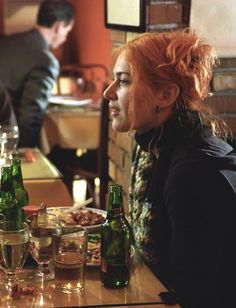 a woman with red hair sitting at a table in front of some bottles and glasses