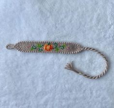 a beaded bracelet with an orange and green flower on the end is laying on a white surface