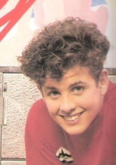 a young man with curly hair smiling at the camera in front of a wall mural