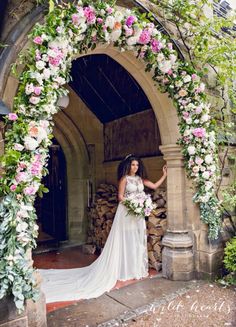 a woman in a wedding dress standing under an arch with flowers