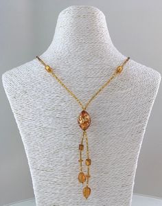 This romantic necklace features Murano glass beads in the following shapes: oval, leaves, cubes and coins.  The central bead measures 20mm (25/32 in.). It encases 24kt gold foil forming abstract patters that glitter in the presence of light.  The cubes also contain 24kt gold foil and measure 6mm (15/65 in.) This necklace is fully beaded with Czech gold-layered seed beads.  As always, the lobster closure and extender chain, 50mm (2 in.), are made of 14kt gold filled* materials. Measurement Conver Handmade Gold Lariat Necklace With Round Beads, Vintage Glass Necklaces With Oval Beads, Vintage Glass Necklace With Oval Beads, Adjustable Czech Glass Necklaces With Dangling Beads, Murano Glass Beaded Necklace As Gift, Adjustable Czech Glass Necklace With Dangling Beads, Gold Oval Bohemian Necklace, Elegant Amber Necklace With Gold Beads, Adjustable Murano Glass Beaded Necklace For Gifts