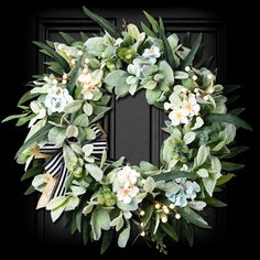 a wreath with white flowers and green leaves is hanging on a black front door frame