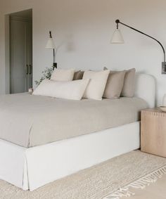 a bed with white linens and pillows in a large room next to a wall lamp