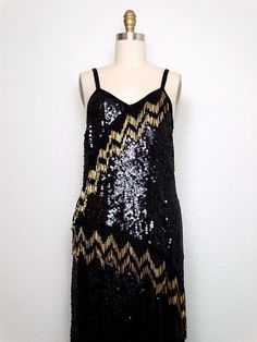 "This is a gorgeous vintage hand beaded dress fully embellished with black sequins and beads and accented with long gold glass beading in 4\" strands in an asymmetrical design. It jingles with movement ... STUNNING!! It's in excellent condition. Bust - 36/38\" Waist - 36/38\" Hips - 38/40\" Length - 34-49\" Tag Size - Large This dress comes from a pet-free and smoke-free home. If you would like more info or have any questions, please don't hesitate to ask!" Sequin Gatsby Dress For Costume Party, Gatsby Style Sequined Dress For Costume Party, Festive Gatsby Style Sequin Dress, Vintage Sequined Flapper Dress For Party Season, Glamorous Black Sequined Flapper Dress, Holiday Sequin Flapper Dress For Costume Party, Gatsby Style Embellished Sequin Cocktail Dress, Holiday Sleeveless Flapper Dress With Sequins, Gatsby Style Sequin Party Dress