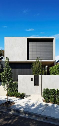 a modern house with trees and bushes on the sidewalk in front of it's entrance