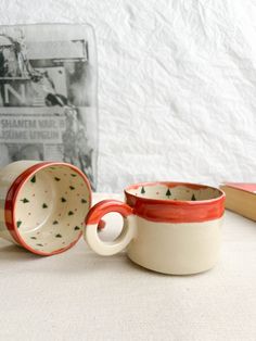 two red and white mugs sitting on top of a table next to a book