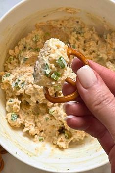 a hand holding a pretzel in front of a bowl of food