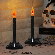 two black candles sitting on top of a table next to a skull