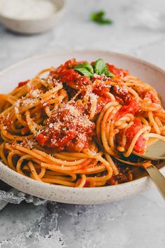 a white bowl filled with spaghetti and sauce on top of a marble table next to a silver spoon