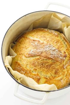 a baked bread in a pot on a white table with some parchment paper around it