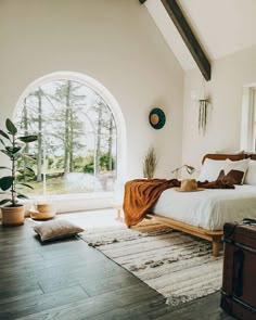 a bedroom with a large arched window and wooden bed in the middle, along with an area rug on the floor