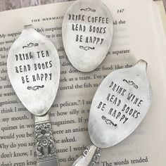 three spoons with words on them sitting on top of an open book that says drink tea, read books, be happy