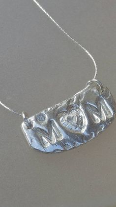 "Handmade by Alison and finished by yours truly. Monstera Leaf background. Mom with heart inside a heart for the \"O\". Lots of texture with this pendant. Solid sterling silver. Comes with matching Cardano style chain in 18 inches. Pendant has two jump rings. Pendant measures approximately half an inch top to bottom at center and just over an inch wide. Cursive Mom on back. Perfect give for your favorite mom." Sterling Silver Heart Pendant Name Necklace For Mom, Sterling Silver Heart Necklace For Mother's Day, Silver Heart Necklace For Mom, Everyday Engraved Silver Heart Necklace, Handmade Silver Heart Necklace For Mom, Silver Engraved Heart Necklace For Everyday, Silver Heart Necklace For Everyday And Mother's Day, Silver Necklace With Heart Charm As Gift For Mom, Silver Heart Pendant Necklace For Mom