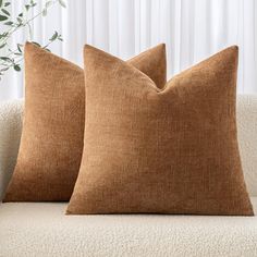 two brown pillows sitting on top of a white couch next to a potted plant