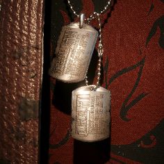 two silver dog tags hanging from a chain on a red background with black and white designs