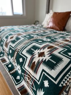 a bed with a green and white blanket on it's headboard next to a window