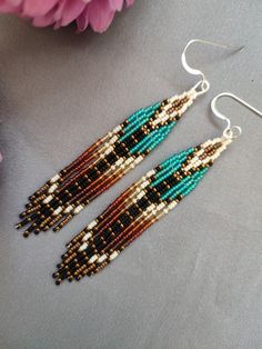 two pairs of beaded earrings on top of a table next to pink flowers and a purple flower