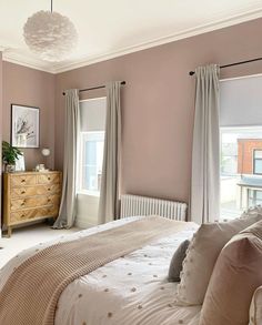 a bedroom with pink walls and white bedding, beige drapes on the windows