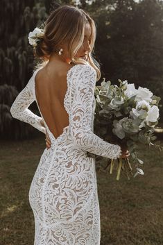 a woman in a white lace wedding dress holding a bouquet and looking at her back