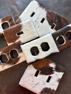 four brown and white cow hide switchplates laying on top of each other with holes in them