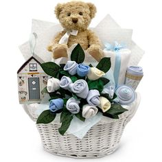 a teddy bear sitting on top of a white basket filled with baby stuff and flowers