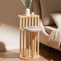 a corner table with a book and vase on it next to a couch in a living room