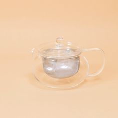 a clear glass teapot with a lid on a beige background, filled with water