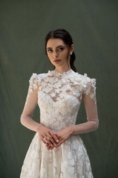 a woman wearing a white dress with flowers on the neck and sleeves, standing in front of a green background