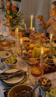 a group of people sitting around a table with food and candles in the middle of it