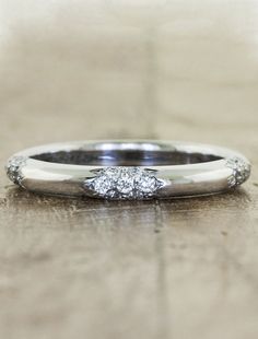 a white gold and diamond wedding ring sitting on a wooden table with light shining in the background