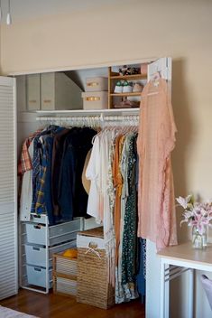 an organized closet with clothes hanging on the rails and baskets in front of it, next to a bed