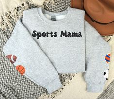 Sports Mama Sweatshirt, Sport Ball Sleeve Sweatshirt, Custom Basketball, Custom Football, Custom Volleyball, Custom Tennis, Custom Soccer, Custom Baseball Mom Shirt These are the perfect sweatshirts for sports moms of all kinds.  You can place the balls on the sleeves that represent the sports your children play. The Gildan sweatshirts are very comfy, and you will want to wear them all season long while curling up with your favorite book and hot beverage.   B R A N D S  We do partner with several providers and use multiple brands of clothing and other products in our shop. We source American and responsibly made products whenever possible.  The following are the current brands we use for our clothing designs: Bella + Canvas  Comfort Colors® Deco (Slides) Gerber Childrenswear Gildan Rabbit Workout Sweatshirt With Letter Print For Sports Season, Letter Print Sweatshirt For Sports Season Workout, Athletic Heather Team Spirit Sweatshirt For Sports, Athletic Heather Team Spirit Sports Top, Varsity Long Sleeve Sweats For Sports, Team Spirit Moisture-wicking Sweatshirt For Sports Events, Varsity Crew Neck Sweatshirt For Sports, Athleisure Team-colored Sweatshirt For Sports Season, Sporty Sweatshirt For Sports Season