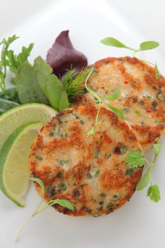 two crab cakes on a white plate topped with green garnish and lime wedges