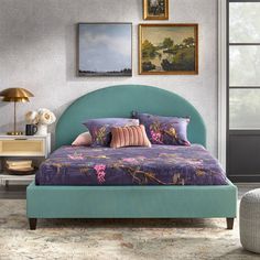 a green bed with pink and purple pillows in a gray room next to pictures on the wall