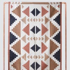 a white and brown blanket hanging from a copper frame on the wall with an arrow design