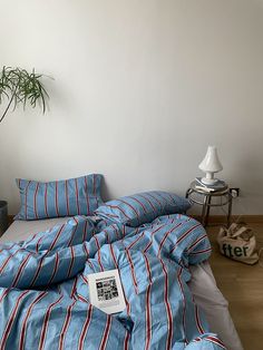 a bed with blue and red striped comforter next to a potted plant on the floor