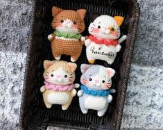 four small crocheted cats sitting in a basket on the ground next to each other