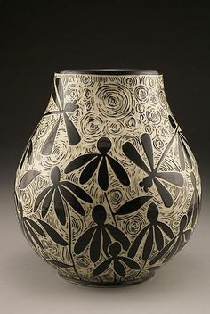 a black and white vase with dragonflies on it's sides, sitting in front of a dark background