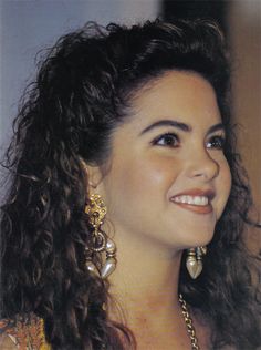 a close up of a person with long hair wearing earrings and smiling at the camera