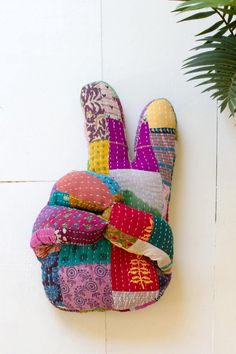 a multicolored patchwork glove hanging on the wall next to a potted plant