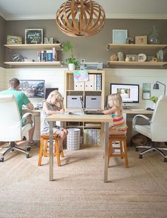 two people sitting at a desk in front of computer monitors and laptops with shelves above them