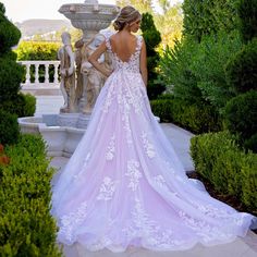 a woman in a pink wedding dress standing next to some bushes and trees with her back turned towards the camera