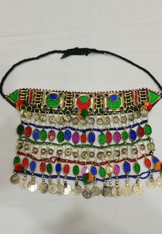 * This traditional classic necklace is an epitome of tradition. The tribal choker statement features three layers, each embellished with multicolour glass stones. * The style of the necklace is inspired by the Kuchi style of ornaments, as adorned with floral motifs and vintage coins dangling at the bottom. * The golden silver hues are complementing the vibrant glass stone inlays and elements at the top and bottom. The tribal necklace is a traditional fashion jewelry statement, festooned with met Multicolor Metal Necklaces For Celebration, Multicolor Necklace For Festival Gift, Handmade Necklaces For Festivals, Bohemian Multicolor Beaded Necklaces For Traditional Ceremonies, Colorful Beads Jewelry For Festival Gift, Multicolor Beaded Jewelry For Rituals, Colorful Beaded Jewelry For Festival Gift, Festival Jewelry With Colorful Beads As Gift, Festival Jewelry With Colorful Beads For Gift